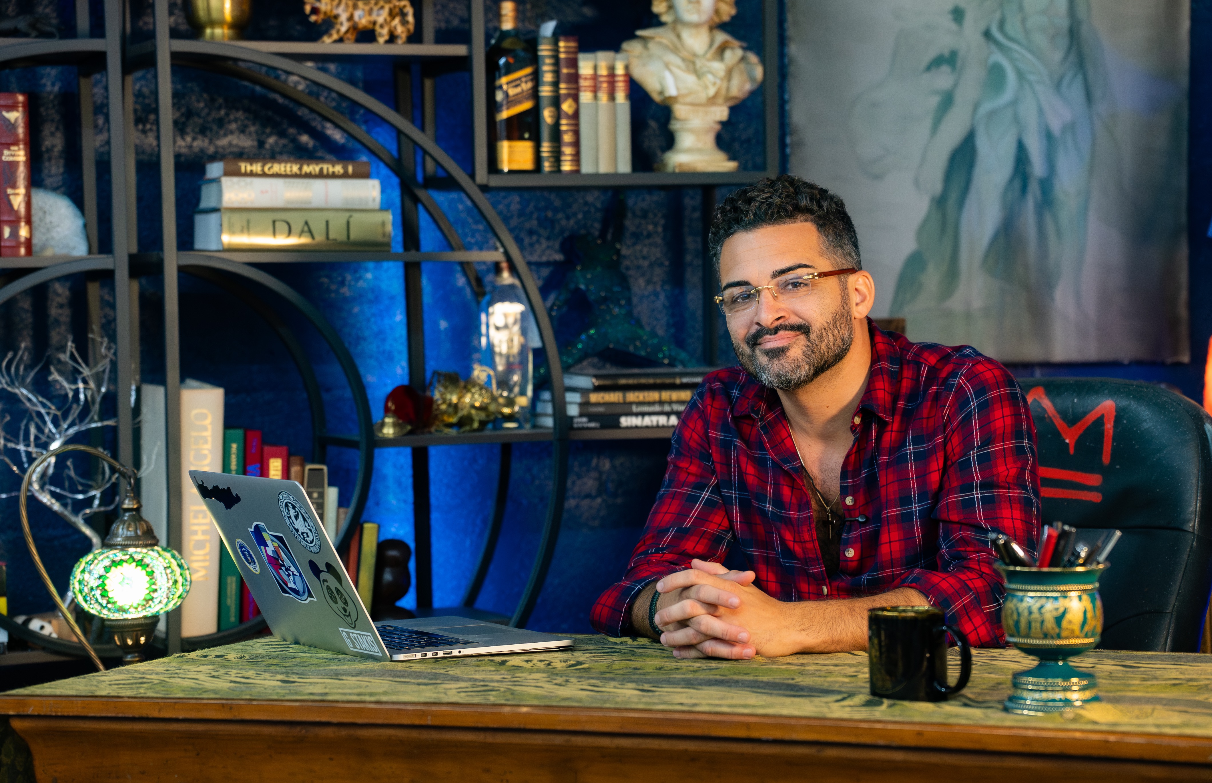 Portrait of the artist GSTAKIS seated in his studio surrounded by books, a classical bust, and iconographic works.